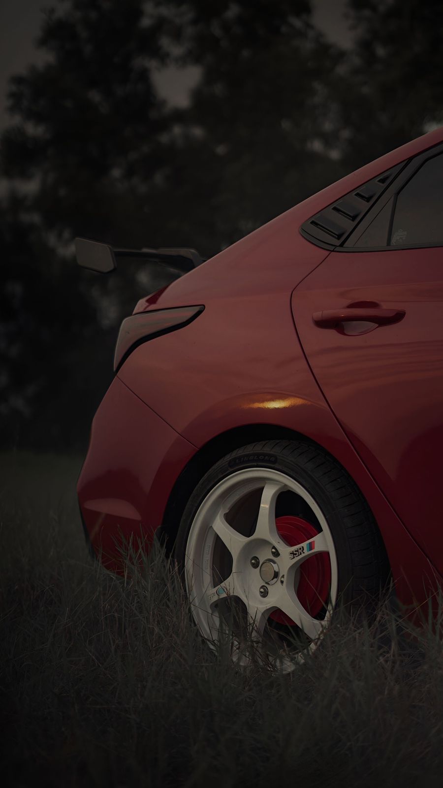 The freshly corrected red paintwork of a car standing on wet tarmac at night