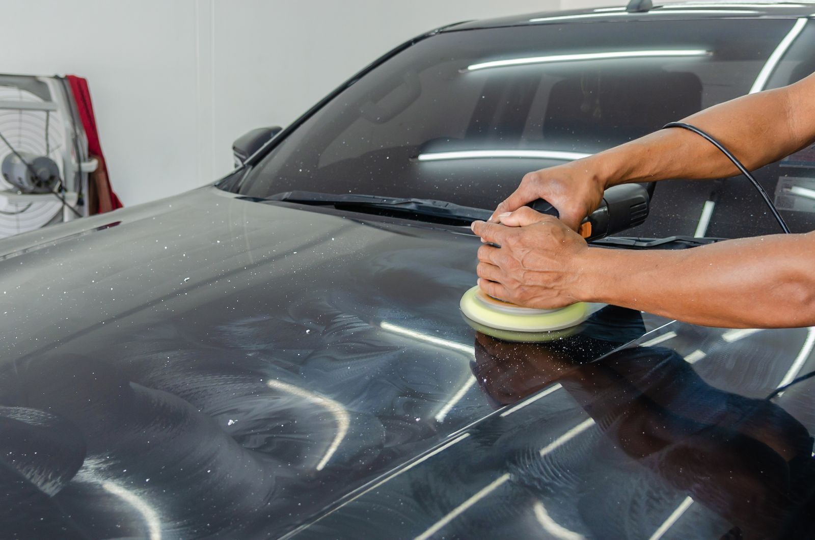 A detailer's hands polishing the bonnet of a dark car with a foam pad
