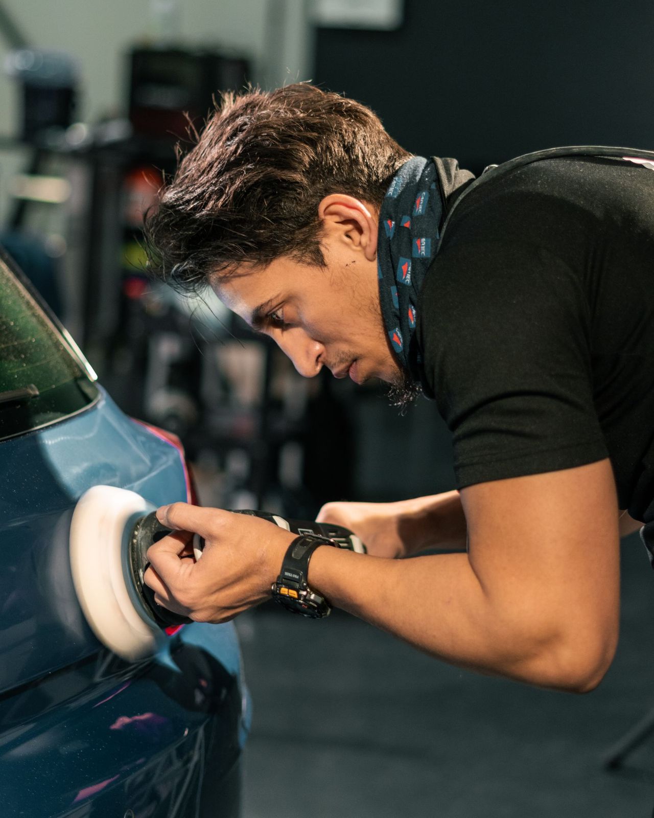 A technician machine-polishing the front wing of a blue car