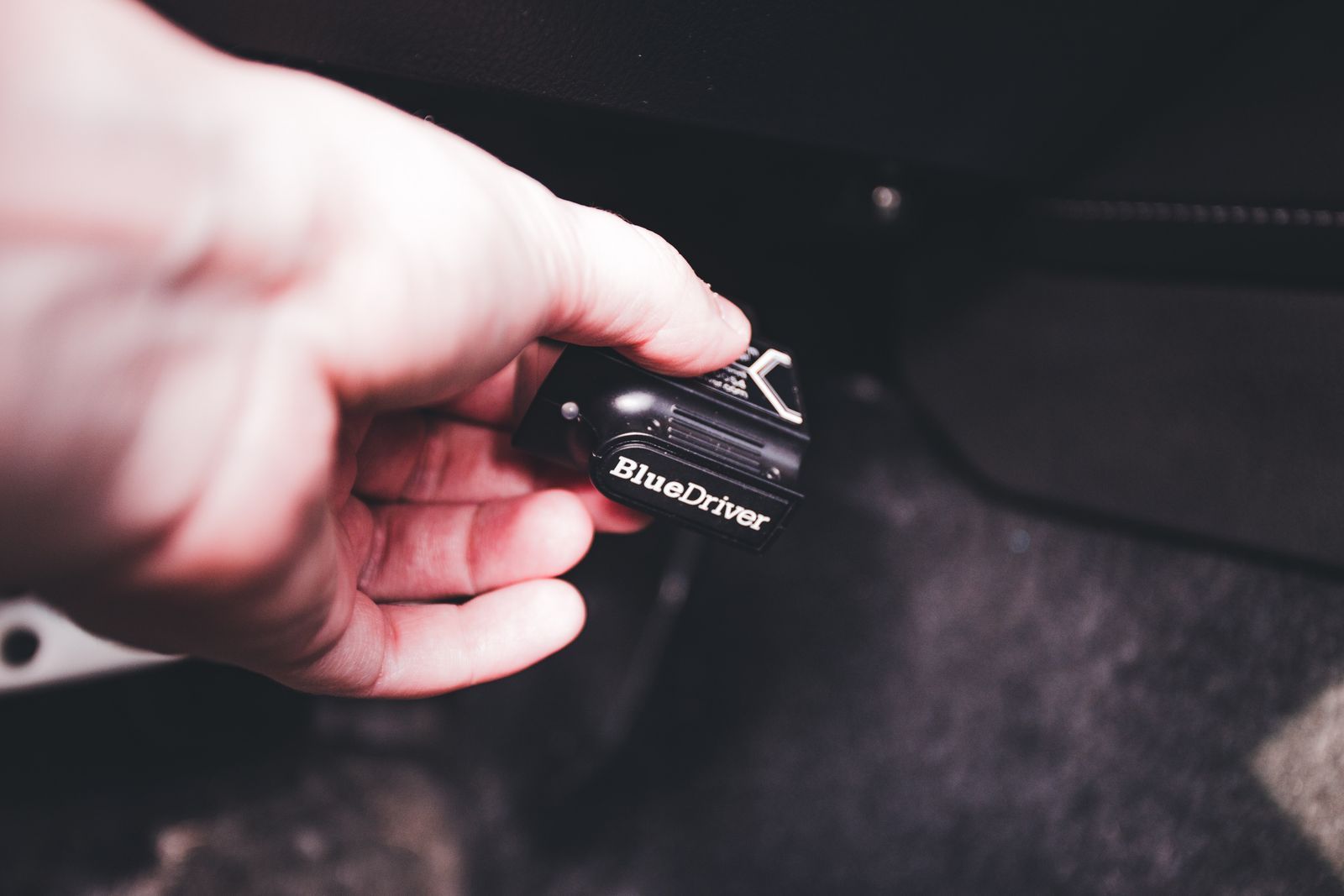 A hand holding a diagnostic handset that is plugged into a car's diagnostics port