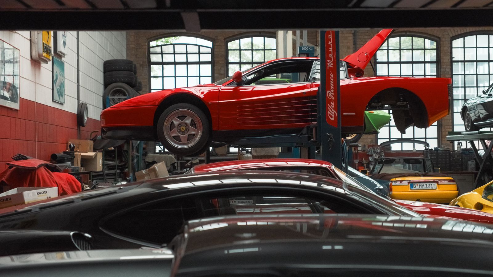 A classic red sports car on the lift, with other cars behind it in the garage
