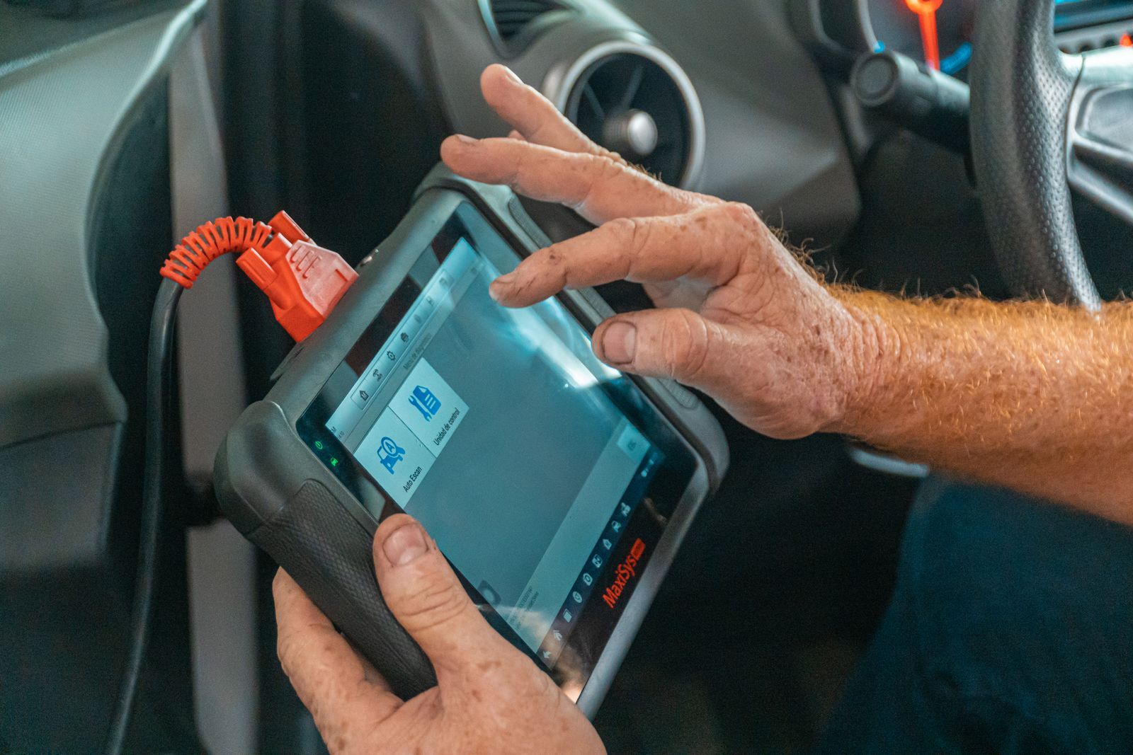 Hands holding a diagnostic tablet plugged into the cabin of a car