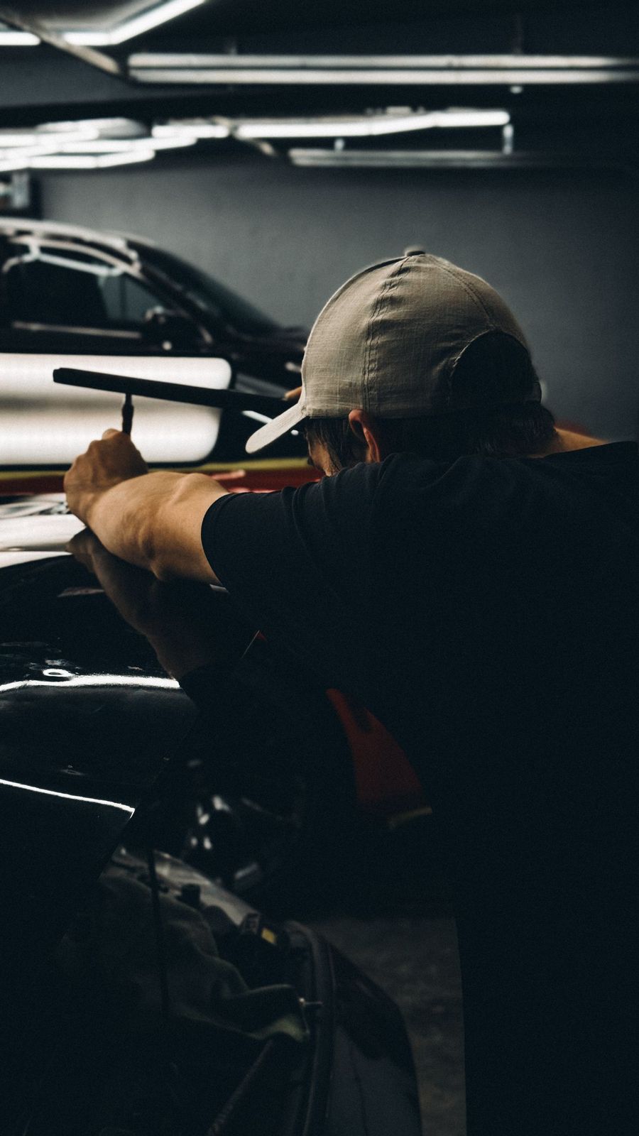 A mechanic leaning into an open engine bay under workshop lights