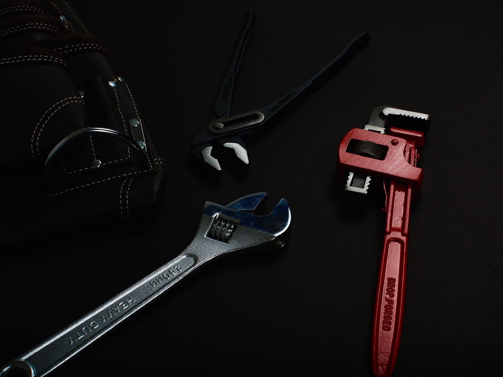 A combination wrench, a pipe wrench and a torch laid out on a dark workshop bench