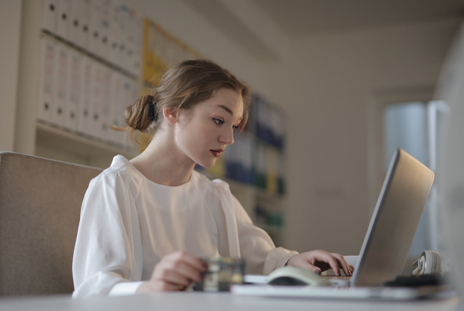 An accountant working on a laptop beside a notebook and printed ledgers