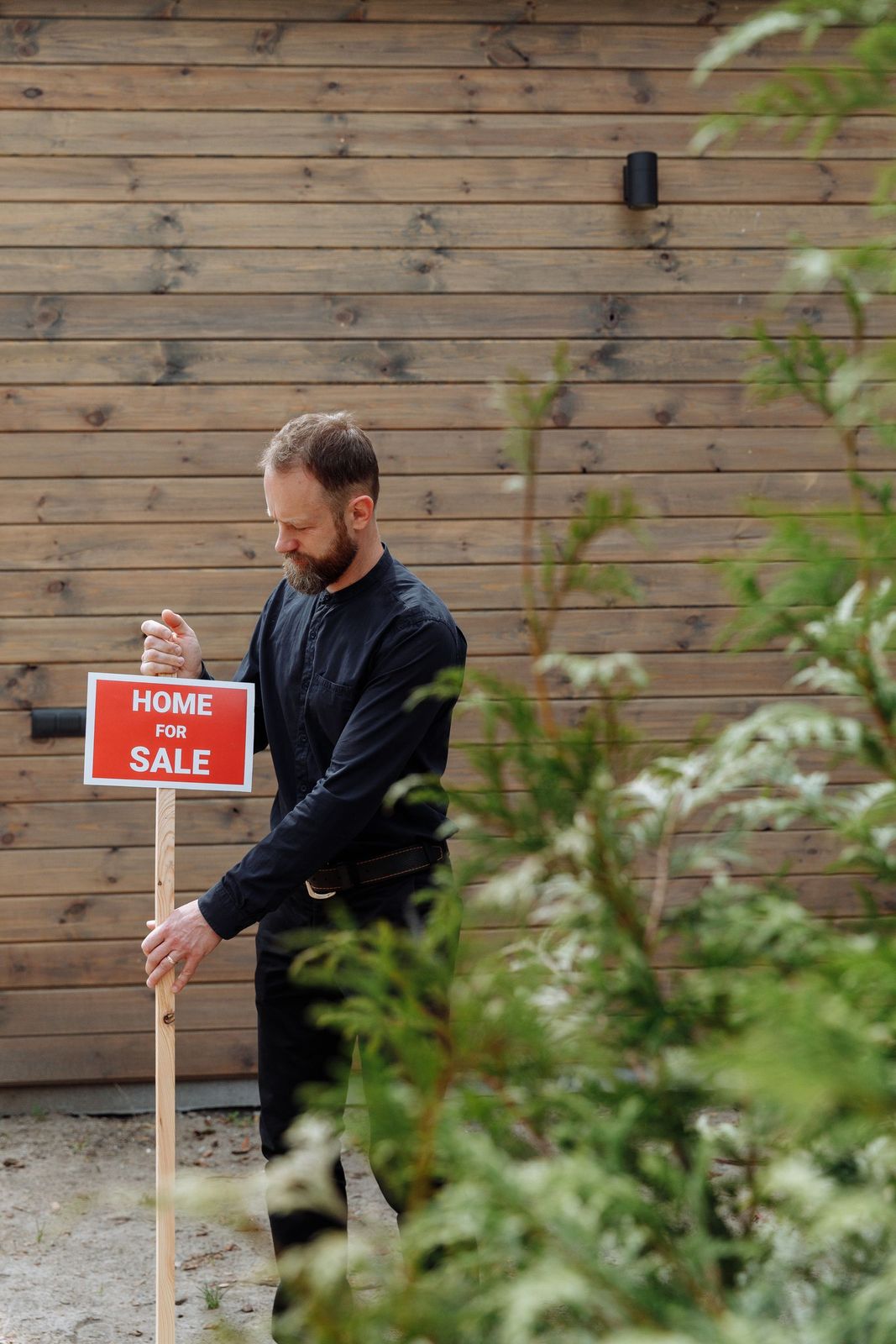A man holding a home-for-sale board outside a timber-clad house