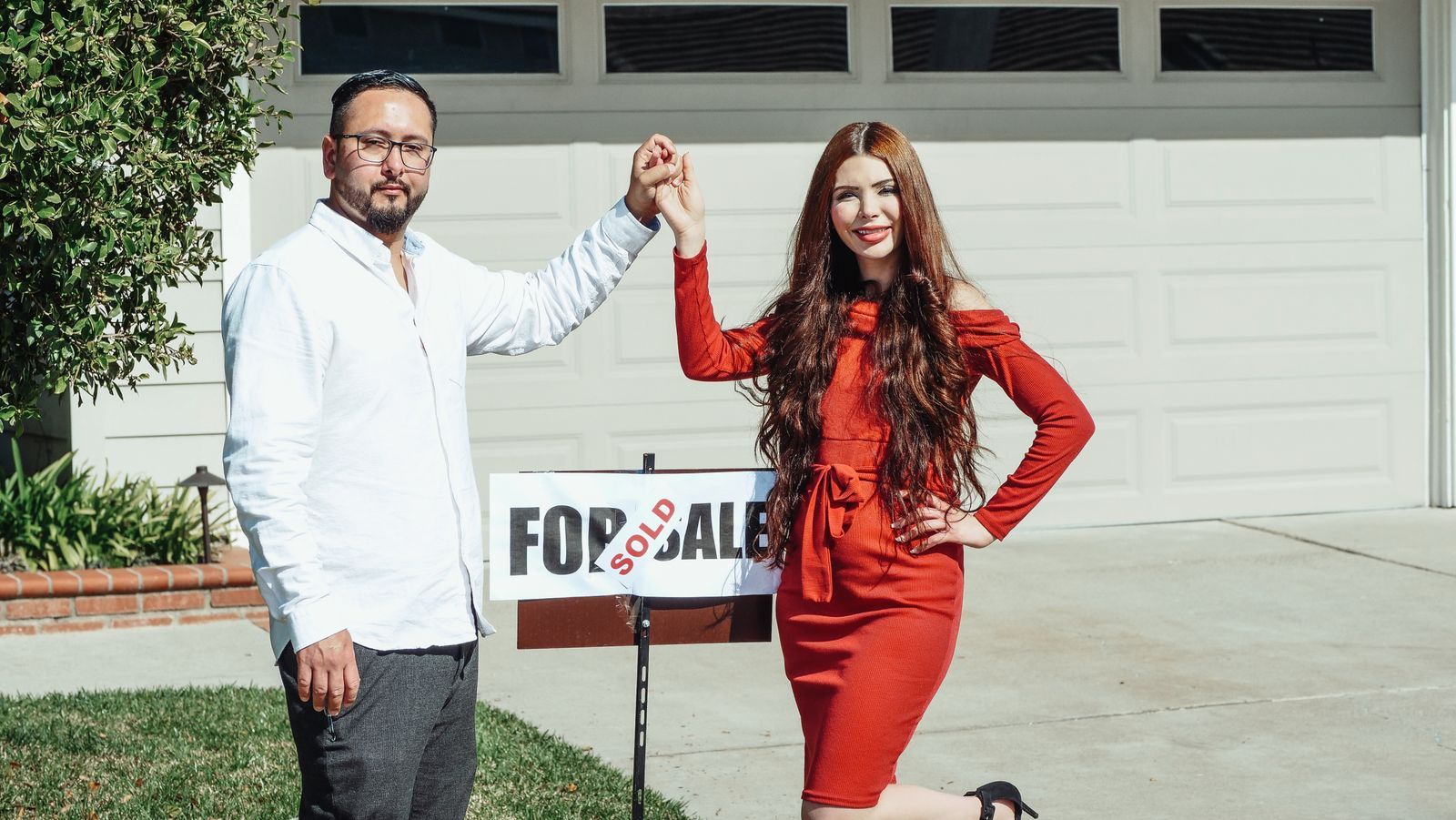 A couple holding a for-sale board outside a property