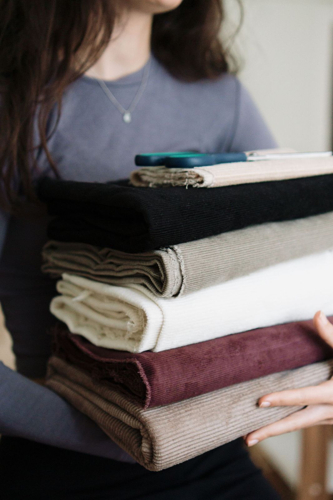 A woman holding a stack of folded linen fabrics against a plain wall